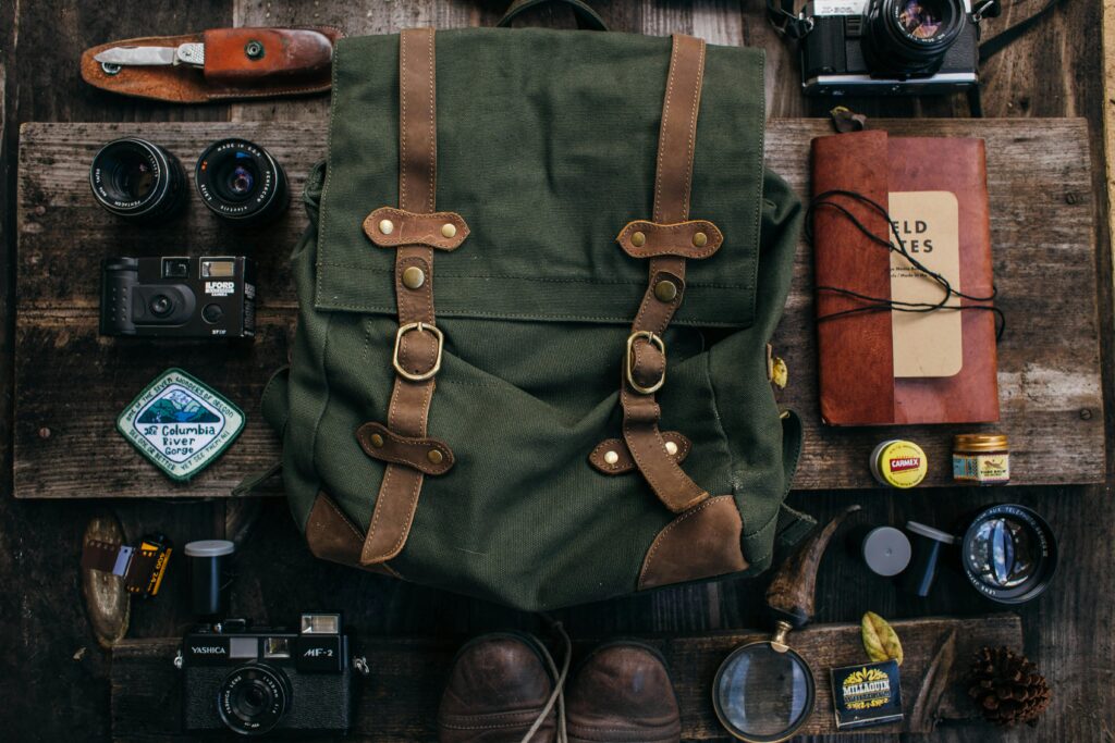 Overhead of backpack near vintage photo cameras near lenses and camera roll near shoes and notebook near knife placed on table